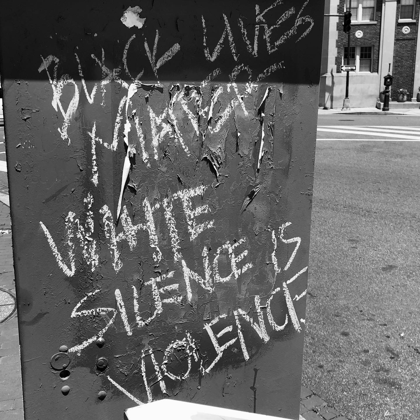 Gros plan d'un panneau, dans une rue, portant l'inscription "Black lives matter, White silence is violence" à la craie en lettres majuscules.
